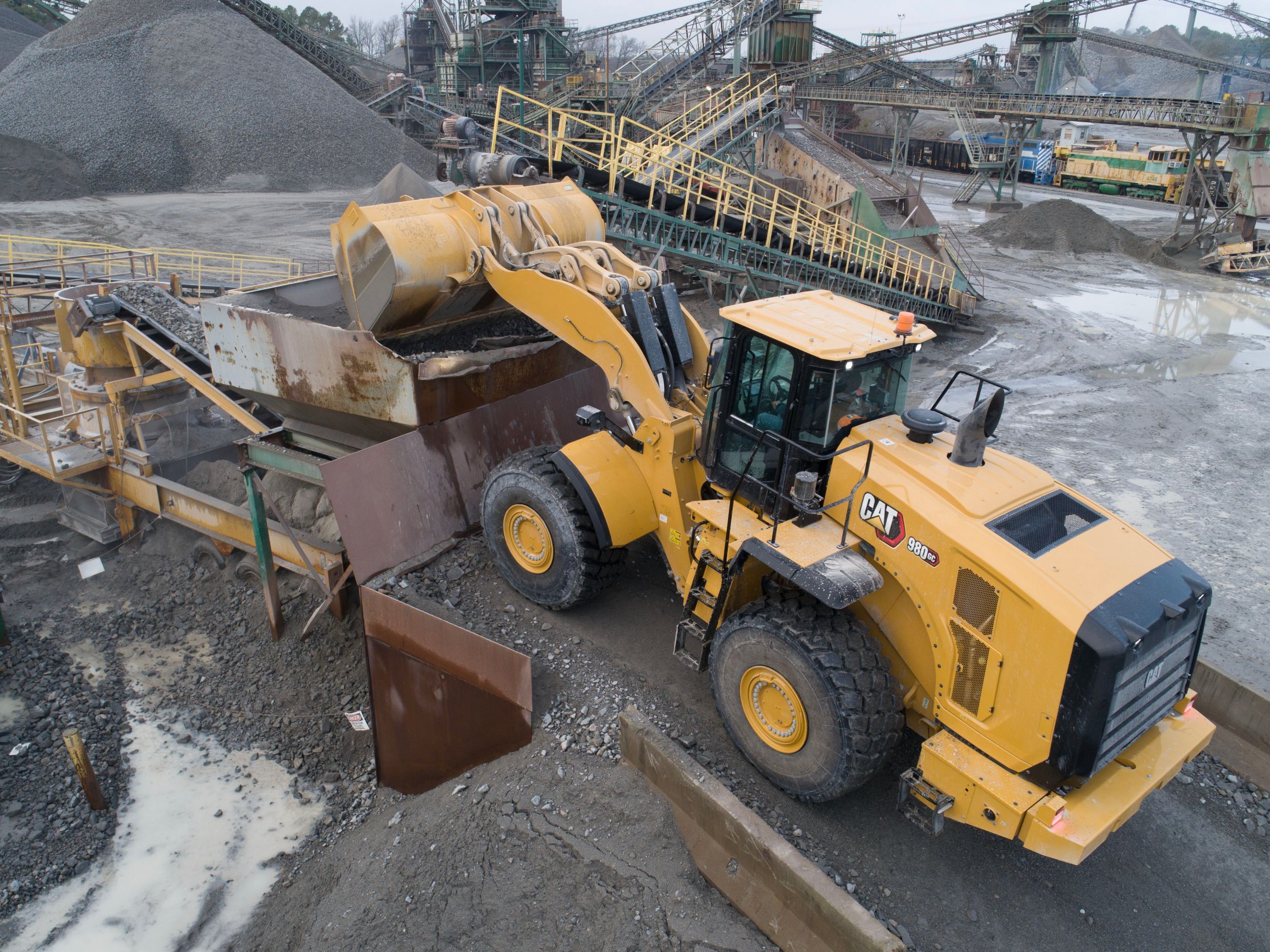 The Cat 980 GC wheel loader at a construction or mining site is dumping a load of gravel into a hopper.