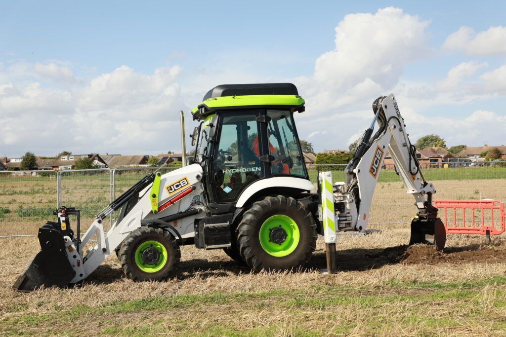 A backhoe loader with white and green livery in a field on against a blue sky with white clouds