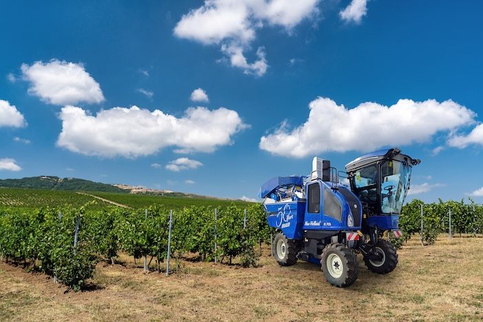 Blue grape harvester in field with 50th anniversary on the side