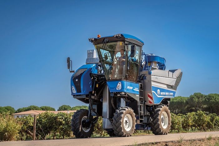 Side view of blue grape harvester vehicle against a blue sky