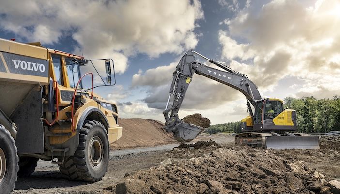 Volvo CE ECR355 short swing excavator loading material into articulated dump truck on construction site under blue sky