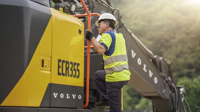 Construction worker in high-visibility safety vest accessing Volvo ECR355 excavator cab via handrail system during site operations