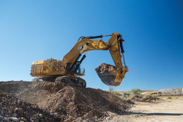 Cat 6015 hydraulic mining shovel operating on rocky terrain with bucket extended during material handling operations