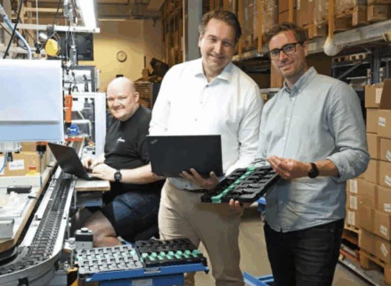 Three TYRI employees in a factory setting with circuit board production equipment