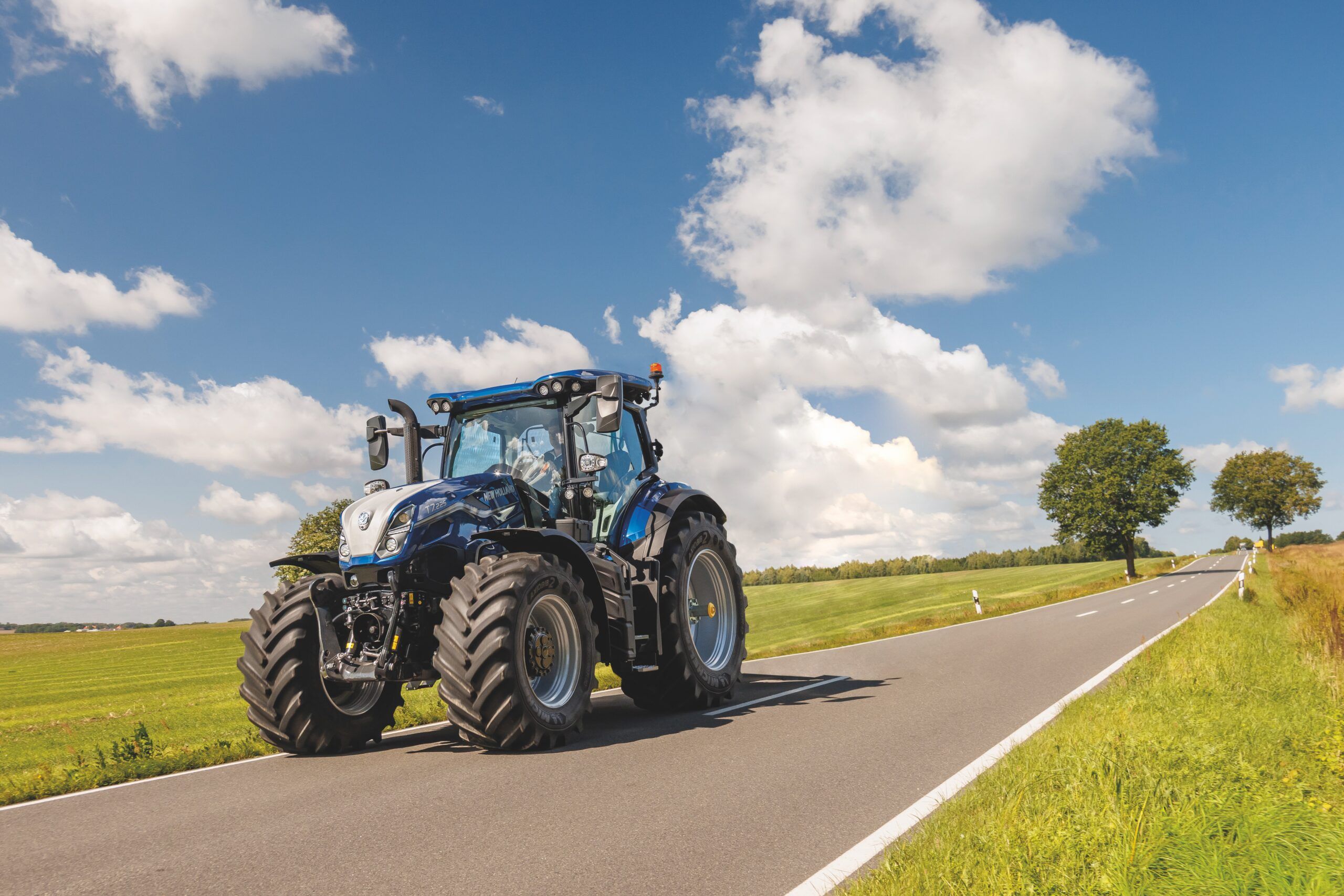 New Holland T7 SWB tractor on road transport between fields, highlighting the model's redesigned cab suspension system and front axle suspension that work together to deliver improved ride comfort and safety during travel over varied terrain.