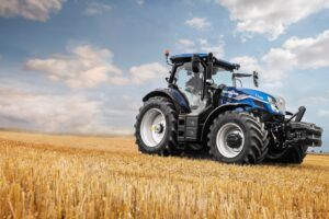 New Holland T7.225 tractor in signature blue livery, positioned in a harvested stubble field against a dramatic cloudy sky