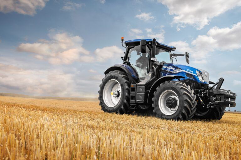 New Holland T7.225 tractor in signature blue livery, positioned in a harvested stubble field against a dramatic cloudy sky