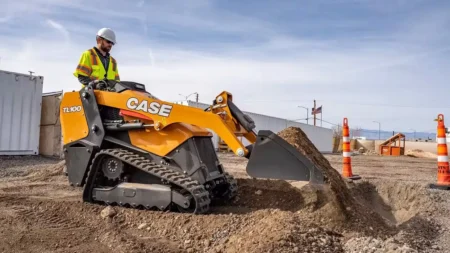 A Case TL100 mini track loader operated by a worker in high-visibility clothing and hard hat, moving material on a construction site