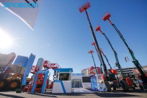 Wide-angle view of the Sinoboom exhibition stand at CONEXPO-CON/AGG 2026, featuring multiple boom lifts extended to full height and scissor lifts on display outdoors under a clear blue sky, with the Las Vegas skyline visible in the background.
