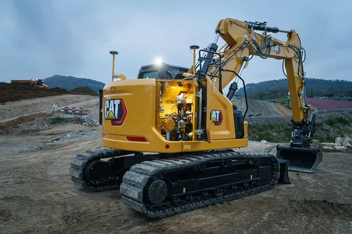 Rear three-quarter view of a Cat 319 at dusk with service doors open and interior lit, showing ground-level maintenance access. GPS receivers are visible on the cab roof and boom.
