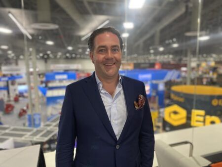 Man in suit and open neck shirt stands in front of blurred out show floor