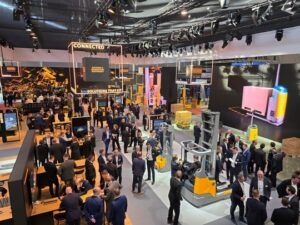 Overhead view of the busy Jungheinrich exhibition stand at LogiMAT 2026, showing visitors browsing displays of forklifts and automated vehicles beneath large overhead signage reading "Connected Solutions That Fit."