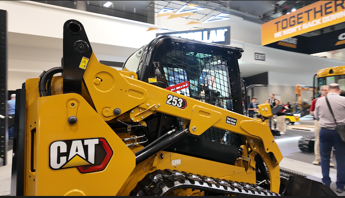 Close-up of the Cat 253 compact track loader on display at CONEXPO-CON/AGG, showing the cab, lift arms, C-Pattern rubber tracks and Two Speed High Flow badging on the bodywork.