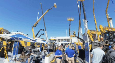 XCMG used ConExpo 2026 platform to push North American expansion Wide-angle view of XCMG's outdoor exhibition stand at CONEXPO 2026 in Las Vegas, showing multiple extended aerial work platforms reaching into a clear blue sky, with excavators and loaders positioned throughout the stand. Visitors and XCMG staff in blue polo shirts are visible throughout the display area, with the XCMG branded pavilion visible in the background.