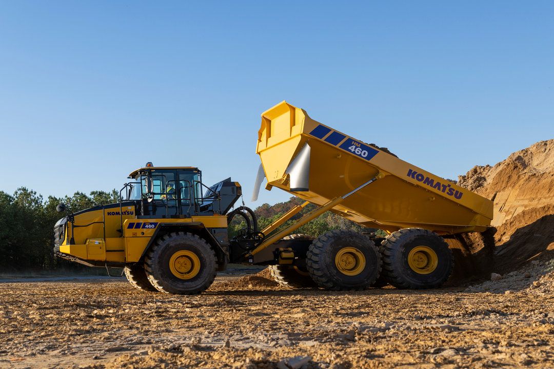 A yellow Komatsu HM460-6 articulated dump truck with its body raised in the tipping position on a dry earthworks site, with a stockpile of material visible in the background.