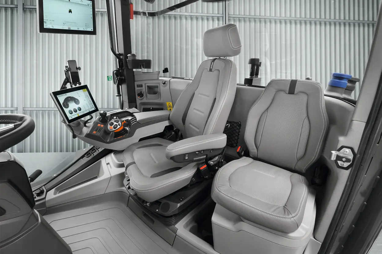Interior of the Claas Xerion 12 cab showing the new luxury driver's seat with armrest-mounted controls and tablet, alongside the passenger seat and steering wheel