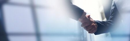 Two business professionals shaking hands in a bright, modern office environment, representing a corporate acquisition agreement between Scanreco and CrossControl.