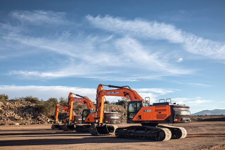 Four orange Develon Series 9 crawler excavators of increasing size arranged in a line on a desert construction site, with mountains in the background