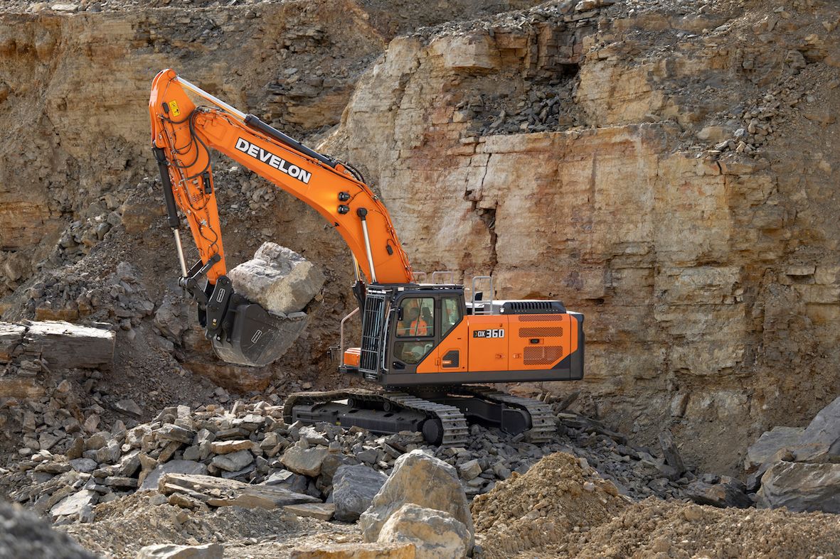 An orange Develon DX360LC-9 crawler excavator handling large rocks in a quarry with exposed rock faces in the background