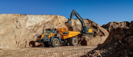 A yellow Hyundai HA45A 4x4 articulated dump truck being loaded with earth by a Hyundai crawler excavator in a quarry