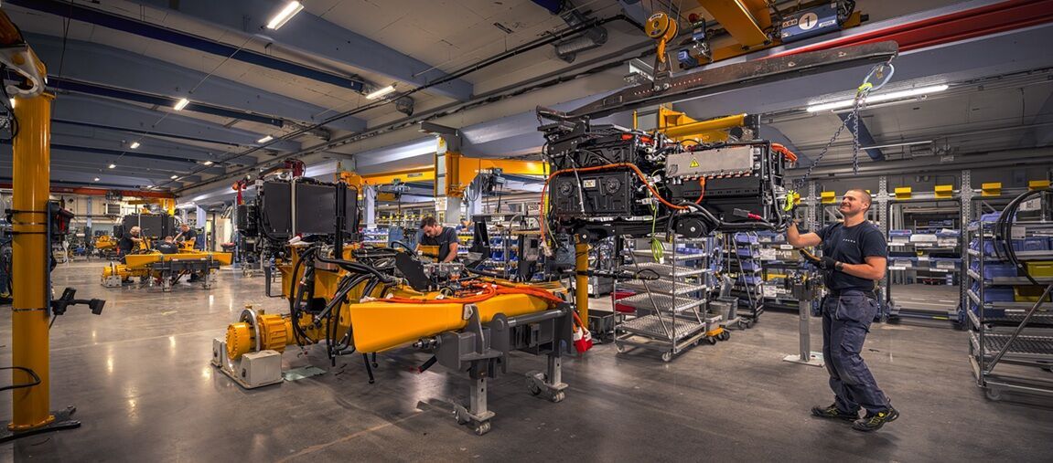 Workers on the production line at Volvo CE's Braås factory assembling components for electric articulated haulers, with partially built machines and overhead cranes visible