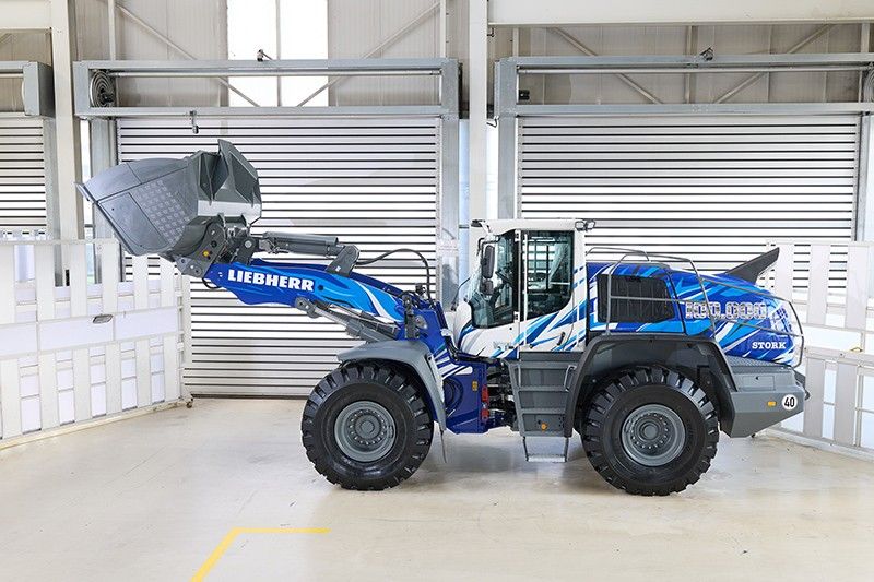 A dark blue Liebherr L 550 XPower wheel loader with commemorative '100,000' graphic livery, displayed inside a warehouse facility