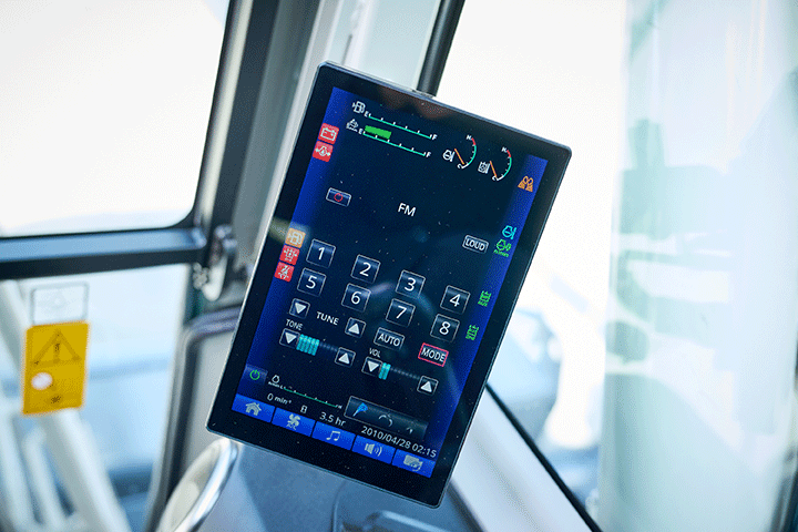Close-up of the 8in. colour touchscreen display inside the Takeuchi TB3150 series excavator cab, showing radio and machine function controls with coloured icons on a dark background