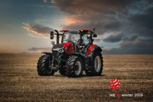 Photograph of a red Case IH Puma 185 tractor in a stubble field at sunset, with a Red Dot Winner 2026 logo in the lower right corner