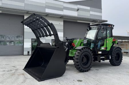 Photograph of a green Sennebogen 360 G telehandler with raised boom, parked outside an industrial building.