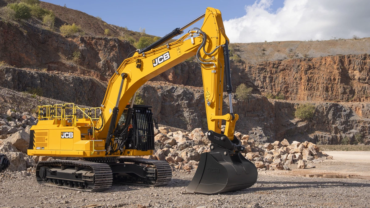 JCB 420X crawler excavator in yellow livery, parked on quarry ground with bucket lowered, against a backdrop of rock faces