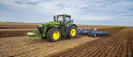 John Deere expands 8R and 8RX series with three high-horsepower models Green and yellow John Deere 8R 540 tractor pulling a blue cultivator across a ploughed field under a cloudy sky