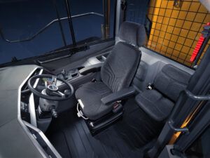 Photograph of the interior of the updated Hyundai articulated dump truck cab, showing the operator seat, steering wheel, central console and a smaller secondary seat to the right.