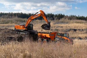 Orange Develon DX400HD-9 crawler excavator loading material into an orange Develon DA30-7 articulated dump truck in an open quarry setting
