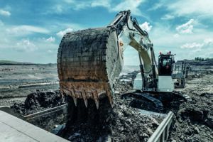 White Liebherr R 9100 mining excavator in backhoe configuration tipping a large bucket of material into a loading area at an open-cast mine