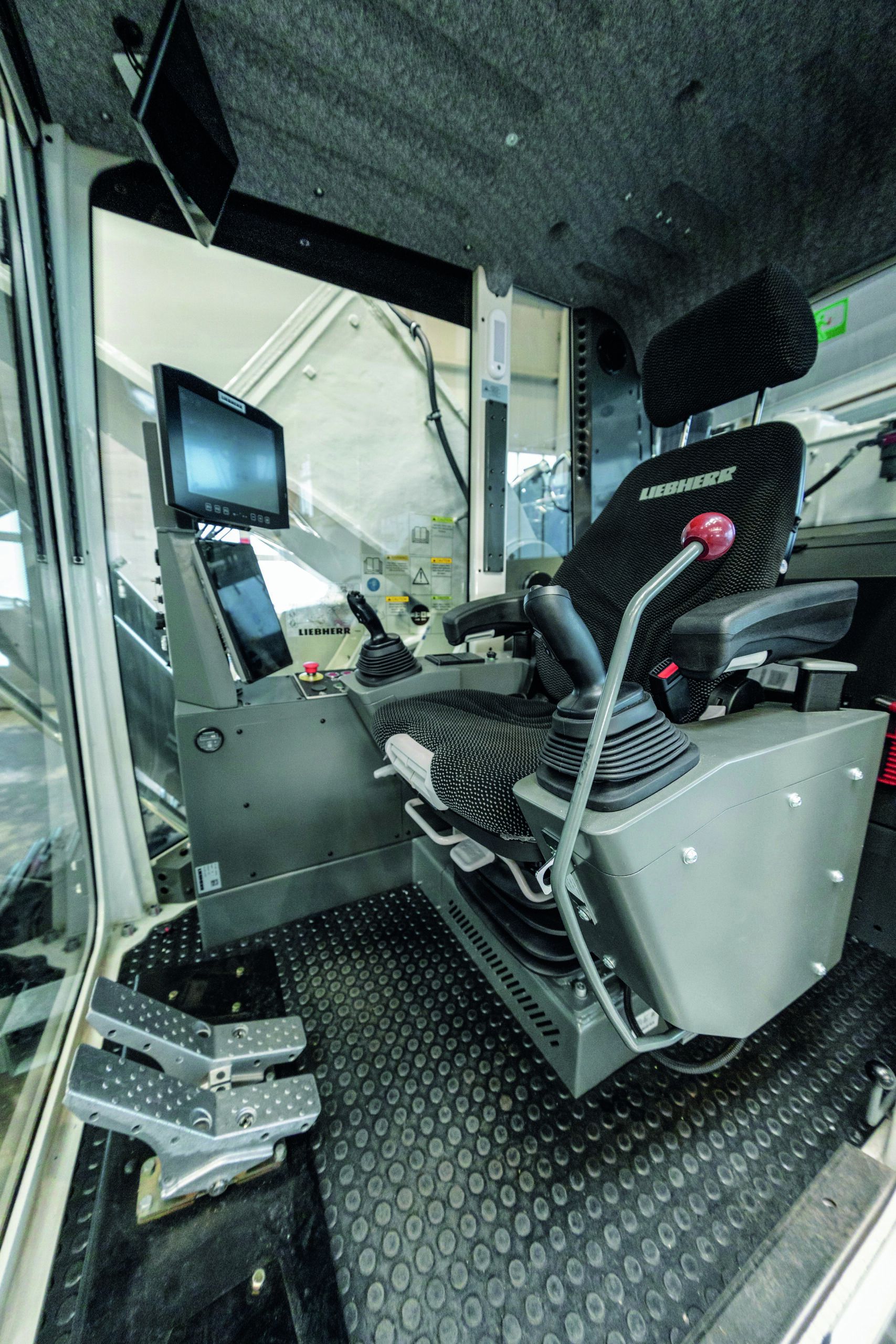 nterior view of a Liebherr mining excavator cab showing the operator's seat, twin joystick controls, a mounted display screen and a secondary overhead monitor