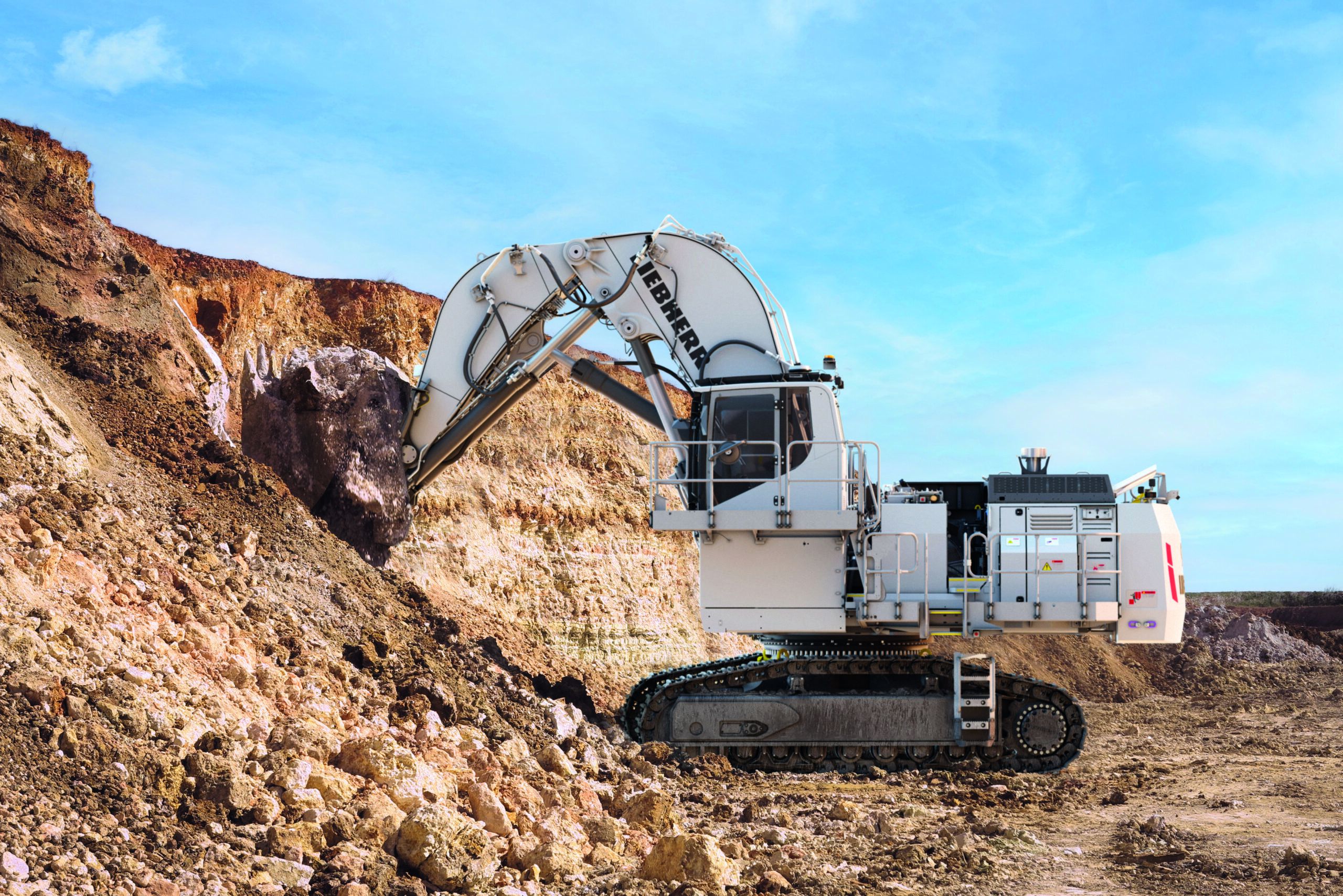 White Liebherr R 9100 mining excavator in face shovel configuration working at a rock face, with boulders and exposed mineral strata visible
