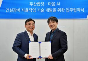 Two men in suits holding a signed MOU document at the Doosan Bobcat and Maum.AI agreement signing ceremony, with a Korean-language banner visible behind them.