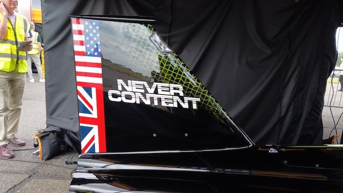 Close-up of the black tail fin of the JCB Hydromax featuring US and UK flags and the words "Never Content" in white lettering