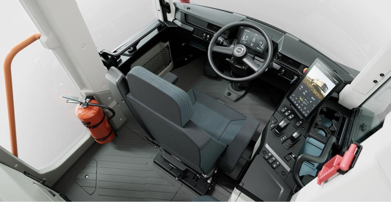 Overhead view of the Volvo A50 cab interior showing the operator seat, steering wheel, touchscreen display and storage, with an orange fire extinguisher visible to the left