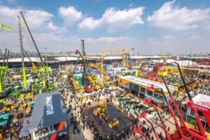 Aerial view of bauma Shanghai exhibition grounds showing large outdoor display of construction machinery including cranes, excavators, and loaders, with the Shantui stand visible in the foreground and extensive crowd attendance.