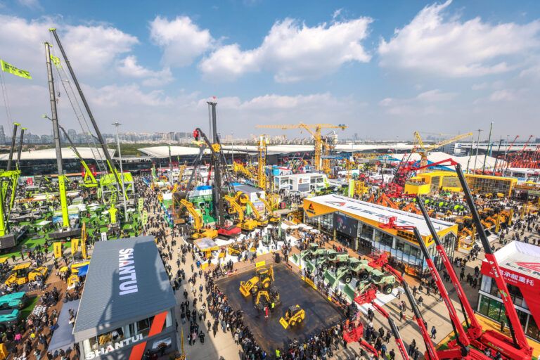 Aerial view of bauma Shanghai exhibition grounds showing large outdoor display of construction machinery including cranes, excavators, and loaders, with the Shantui stand visible in the foreground and extensive crowd attendance.