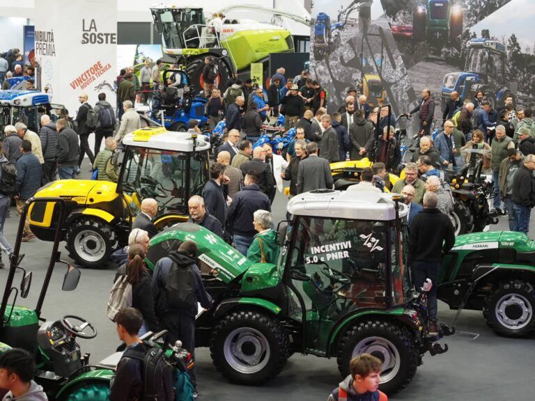 EIMA 2026 confirms 1,800 exhibitors as show grows Busy indoor exhibition hall at EIMA with yellow and green compact tractors and visitors browsing stands