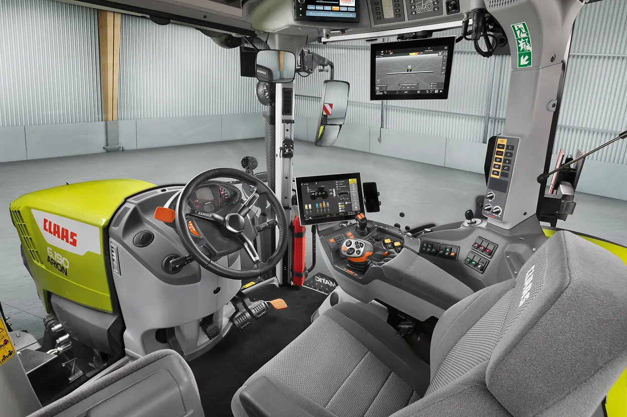 The interior cab of a Claas Arion 6.190 tractor, showing the steering wheel, seat, terminal screens and control lever.