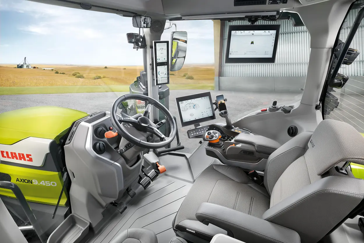 The interior cab of a Claas Axion tractor, showing the steering wheel, seat, terminal screens and armrest control