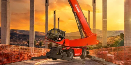 Magni TH expands rotating telehandler lineup Red Magni RTH 8.46 TC rotating telehandler with boom raised and stabilisers down, on a construction site among concrete piers at sunset