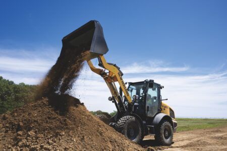New Holland Construction expands D-Series compact wheel loader range Yellow New Holland W80D compact wheel loader dumping soil from a raised bucket onto a mound