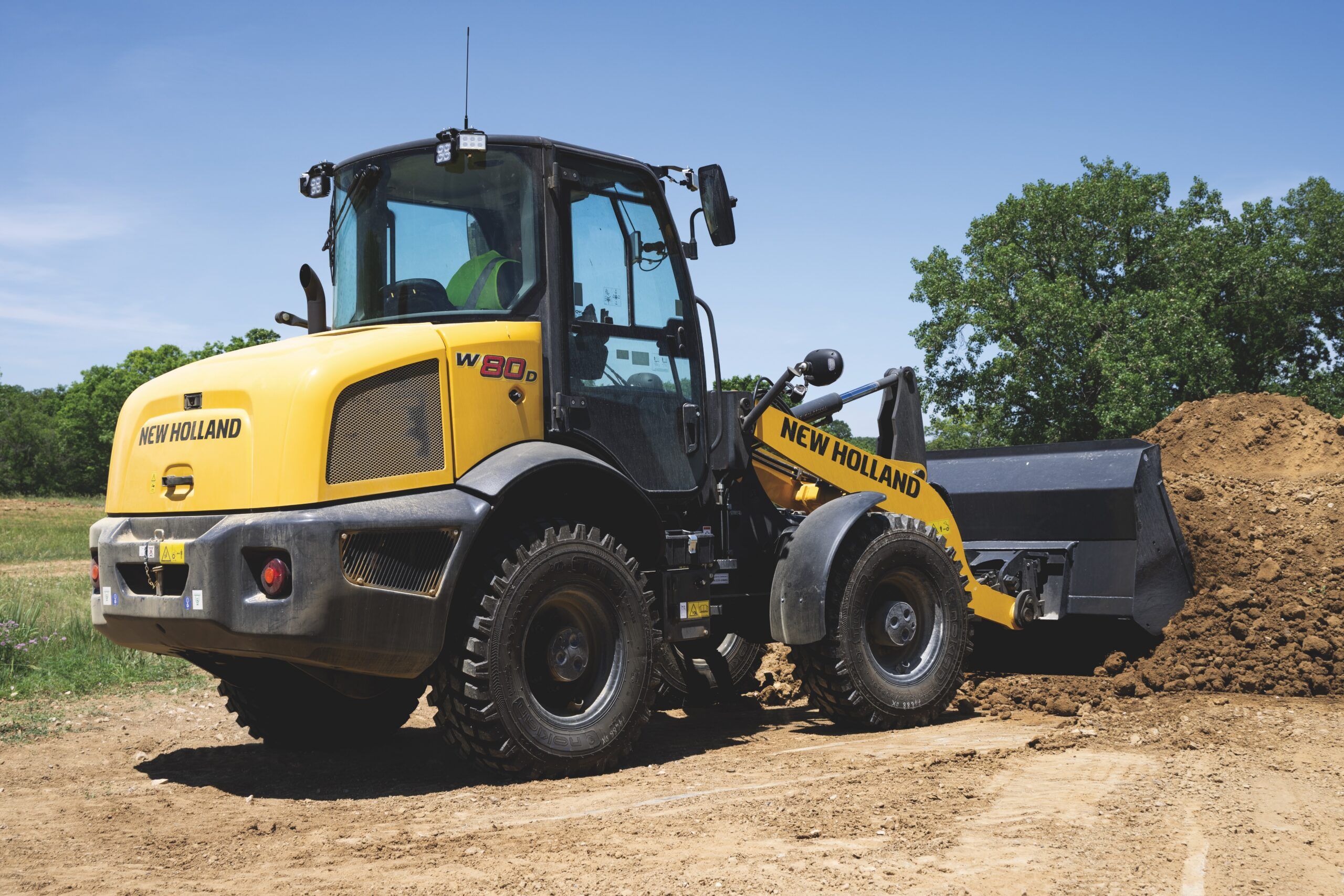 New Holland W80D compact wheel loader with a loaded bucket on a rural worksite