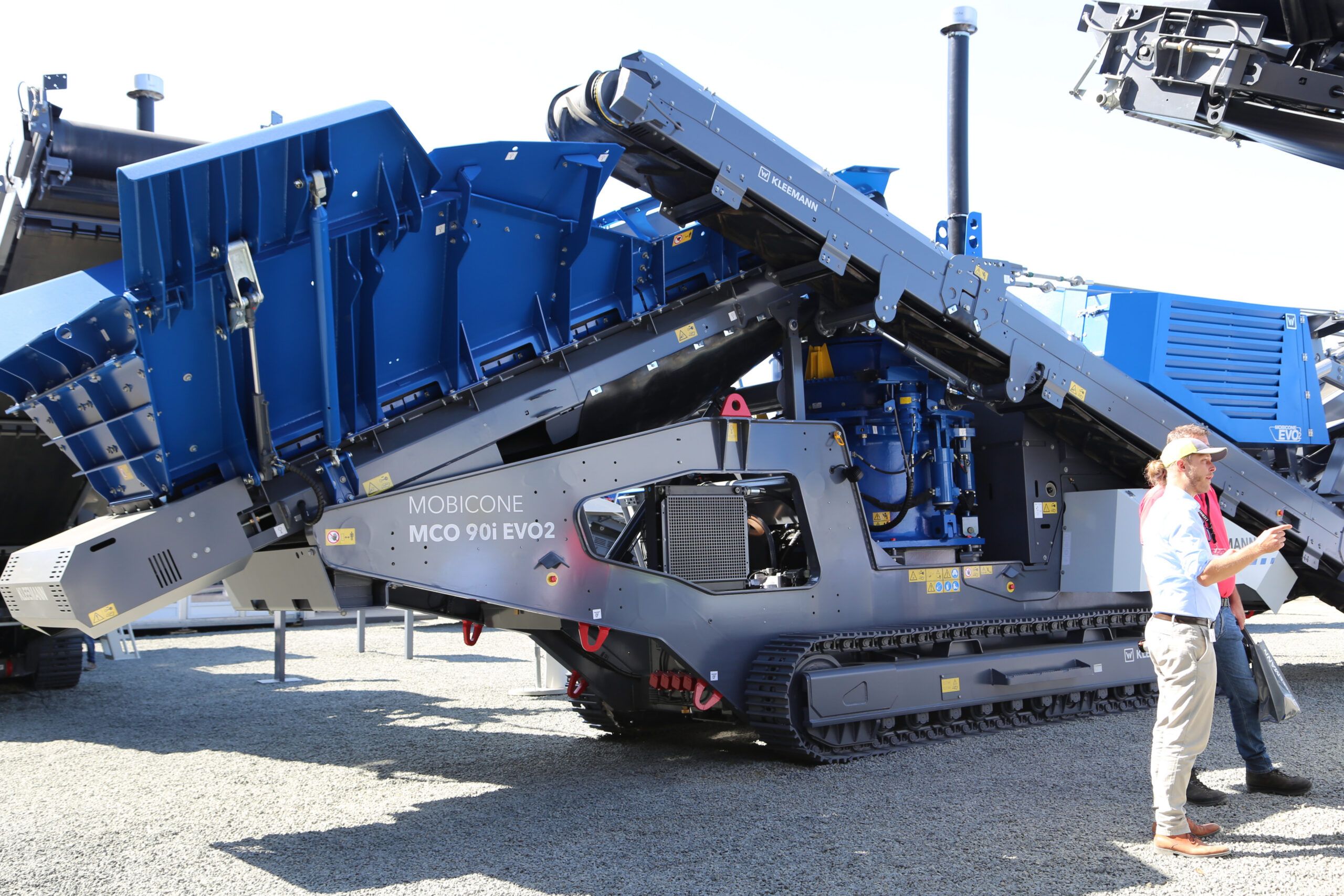 A Kleemann Mobicone MCO 90i EVO2 cone crusher on a show stand, with a visitor standing alongside for scale.