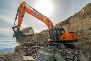 Orange Develon DX400HD-9 crawler excavator lifting a large boulder in a rocky quarry