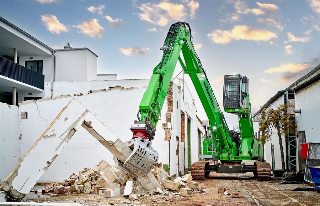 Green Sennebogen demolition excavator carrying out selective demolition of a building in a confined urban setting.